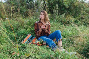 Kıllı papatya çiçekli güzel bir kadın çimenlerde oturup dışarıda çay içiyor.