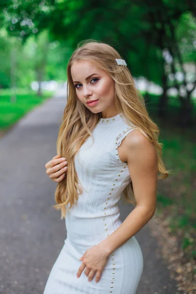 Retrato de una encantadora mujer rubia con hermoso vestido blanco de pie en la carretera bajo los árboles . —  Fotos de Stock