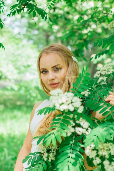 Portret van een charmante blonde vrouw met mooie witte jurk naast een zwanenboom met witte bloemen. — Stockfoto
