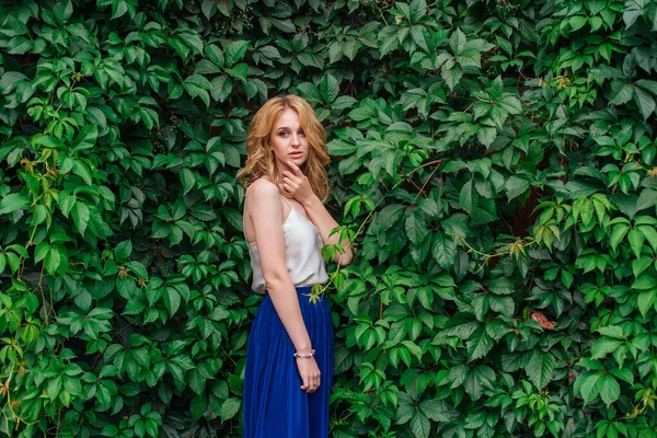 Portret van een jonge mooie vrouw, staande naast de muur van wilde druivenbladeren. — Stockfoto