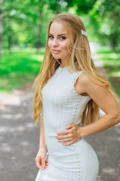 Retrato de una encantadora mujer rubia con hermoso vestido blanco de pie en la carretera bajo los árboles . —  Fotos de Stock