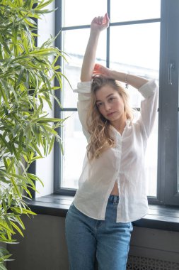 Pencerenin yanında duran genç, güzel sarışın kadın.