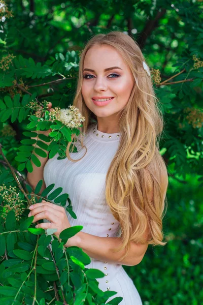 Retrato de uma mulher loira encantadora vestindo belo vestido branco em pé ao lado de Rowan árvore . — Fotografia de Stock