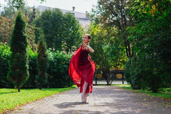 Kvinna ballerina i röd balett klänning dans i pointe skor i höstparken. — Stockfoto