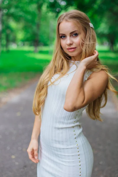 Retrato de una encantadora mujer rubia con hermoso vestido blanco de pie en la carretera bajo los árboles . —  Fotos de Stock