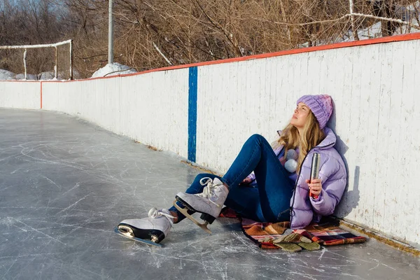 Belle jeune femme relaxante après avoir chevauché des patins à glace et bu une boisson chaude du termo pot sur la patinoire . — Photo