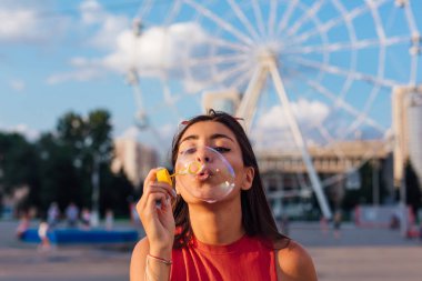 Güzel, genç esmer kadın gün batımında sabun köpüğü üflüyor.