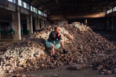 Pembe saçlı genç bir kız çöken bir binada, tuğlaların üzerinde oturuyor.