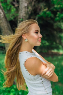 Güzel beyaz elbiseler giyen çekici bir sarışının bahar portresi. Parktaki Rowan ağacının yanında çimlerin üzerinde duruyor..