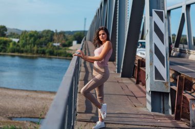 Gün batımında nehrin üzerindeki eski paslı nakliye köprüsünde poz veren genç ve güzel bir kadının ılık yaz portresi..