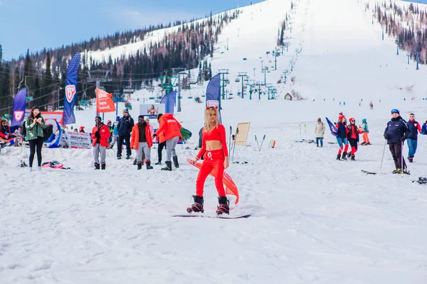 Sheregesh, región de Kemerovo, Rusia - 12 de abril de 2019: Joven mujer bonita feliz vestida con el disfraz de carnaval de un diablo rojo montado en una tabla de snowboard en una pendiente de nieve . — Foto de Stock