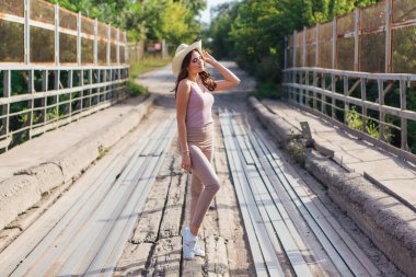 Sıcak yaz portresi, gün batımında eski paslı köprüde kovboy şapkası takan güzel bir kadın..