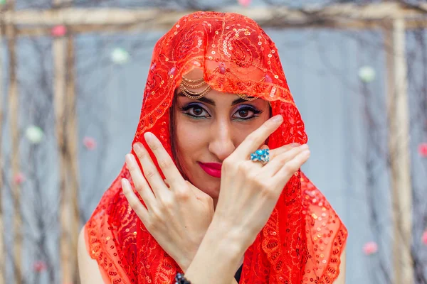 Close up portrait of a beautiful eastern woman with bright makeup and jewelry wearing red headscarf.