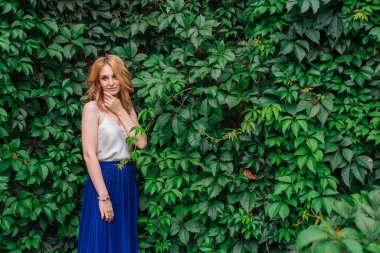 Makyajlı, kıvırcık sarı saçlı, vahşi üzüm yapraklarının yanında duran güzel bir kadının portresi. Boşluğu kopyala.