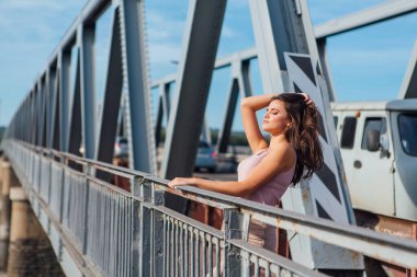 Gün batımında nehrin üzerindeki eski paslı nakliye köprüsünde poz veren genç ve güzel bir kadının ılık yaz portresi..