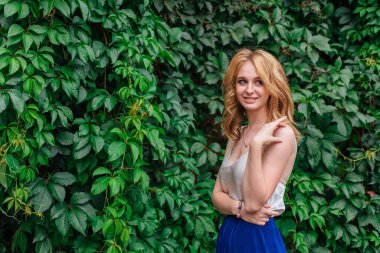 Makyajlı, kıvırcık sarı saçlı, vahşi üzüm yapraklarının yanında duran güzel bir kadının portresi. Boşluğu kopyala.