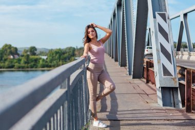 Gün batımında nehrin üzerindeki eski paslı nakliye köprüsünde poz veren genç ve güzel bir kadının ılık yaz portresi..