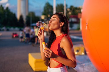 Güzel, genç esmer kadın gün batımında sabun köpüğü üflüyor.