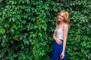 Makyajlı, kıvırcık sarı saçlı, vahşi üzüm yapraklarının yanında duran güzel bir kadının portresi. Boşluğu kopyala.