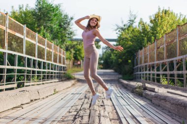 Sıcak yaz portresi, gün batımında eski paslı köprüde atlayan kovboy şapkası takan güzel bir kadın..