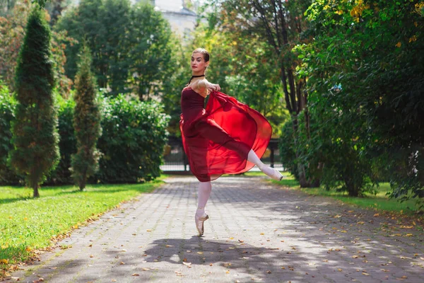 Woman ballerina in red ballet dress dancing in pointe shoes in autumn park. Ballerina standing in beautiful ballet pose