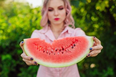 Güzel, gülümseyen, pembe saçlı genç bir kadın ellerinde tatlı bir karpuz tutuyor.