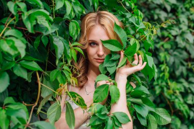 Makyajlı, kıvırcık sarı saçlı, yaban üzüm yapraklarında saklanan güzel bir kadının portresi. Boşluğu kopyala.