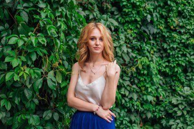 Makyajlı, kıvırcık sarı saçlı, vahşi üzüm yapraklarının yanında duran güzel bir kadının portresi. Boşluğu kopyala.