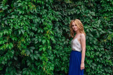 Makyajlı, kıvırcık sarı saçlı, vahşi üzüm yapraklarının yanında duran güzel bir kadının portresi. Boşluğu kopyala.