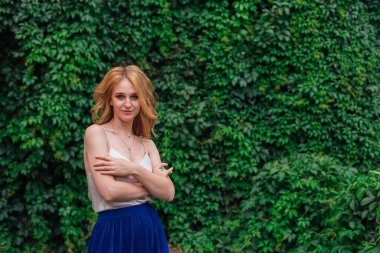 Makyajlı, kıvırcık sarı saçlı, vahşi üzüm yapraklarının yanında duran güzel bir kadının portresi. Boşluğu kopyala.