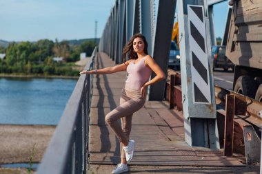 Gün batımında nehrin üzerindeki eski paslı nakliye köprüsünde poz veren genç ve güzel bir kadının ılık yaz portresi..