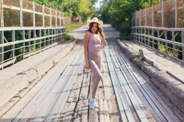 Sıcak yaz portresi, gün batımında eski paslı köprüde kovboy şapkası takan güzel bir kadın..