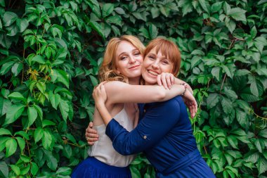 Güzel anne ve yetişkin kızı bir yaz günü yeşil bir arka planda birbirlerine sarılıyorlar.