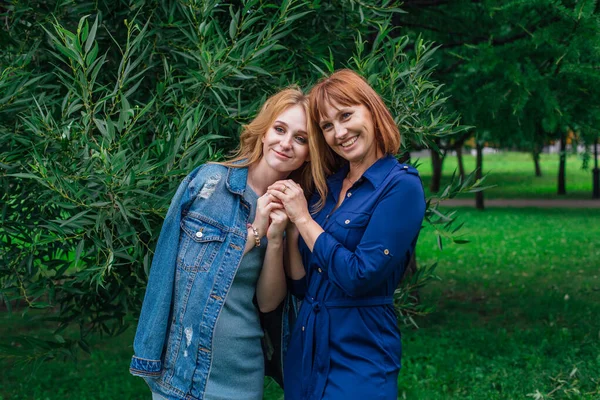 Güzel anne ve yetişkin kızı bir yaz günü yeşil bir arka planda birbirlerine sarılıyorlar.