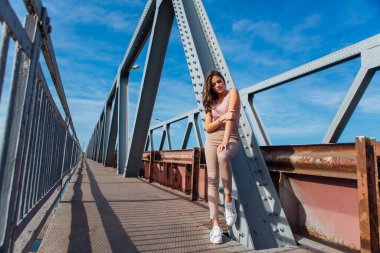 Gün batımında nehrin üzerindeki eski paslı nakliye köprüsünde poz veren genç ve güzel bir kadının ılık yaz portresi..