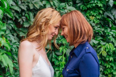 Güzel anne ve yetişkin kızı bir yaz günü yeşil bir arka planda kafa kafaya duruyorlar.