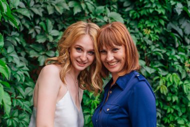 Güzel anne ve yetişkin kızı bir yaz günü yeşil bir arka planda kafa kafaya duruyorlar.