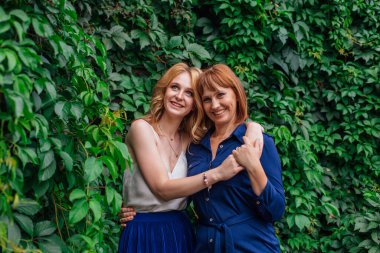 Güzel anne ve yetişkin kızı bir yaz günü yeşil bir arka planda birbirlerine sarılıyorlar.