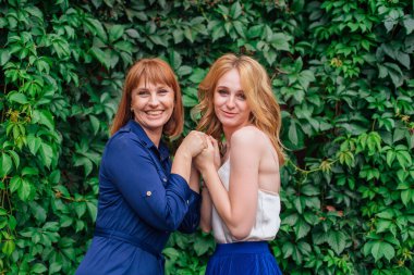 Güzel anne ve yetişkin kızı bir yaz günü yeşil bir arka planda birbirlerine sarılıyorlar.