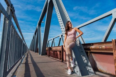 Gün batımında nehrin üzerindeki eski paslı nakliye köprüsünde poz veren genç ve güzel bir kadının ılık yaz portresi..