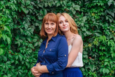 Güzel anne ve yetişkin kızı bir yaz günü yeşil bir arka planda birbirlerine sarılıyorlar.