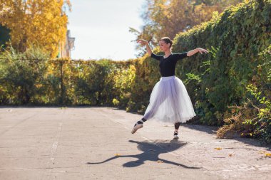 Beyaz etekli kadın balerin altın bir sonbahar parkında sivri ayakkabılarla dans ediyor. Balerin güzel bir bale pozisyonunda duruyor.