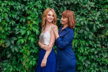 Güzel anne ve yetişkin kızı bir yaz günü yeşil bir arka planda birbirlerine sarılıyorlar.