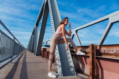 Gün batımında nehrin üzerindeki eski paslı nakliye köprüsünde poz veren genç ve güzel bir kadının ılık yaz portresi..