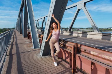 Gün batımında nehrin üzerindeki eski paslı nakliye köprüsünde poz veren genç ve güzel bir kadının ılık yaz portresi..