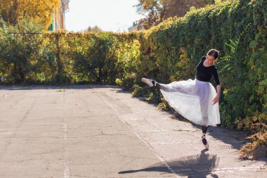 Beyaz etekli kadın balerin altın bir sonbahar parkında sivri ayakkabılarla dans ediyor. Balerin güzel bir bale pozisyonunda duruyor.