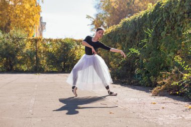 Beyaz etekli kadın balerin altın bir sonbahar parkında sivri ayakkabılarla dans ediyor. Balerin güzel bir bale pozisyonunda duruyor.