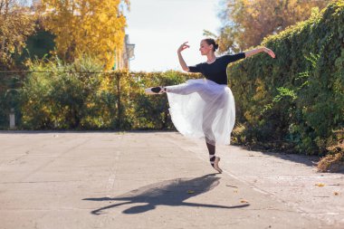 Beyaz etekli kadın balerin altın bir sonbahar parkında sivri ayakkabılarla dans ediyor. Balerin güzel bir bale pozisyonunda duruyor.