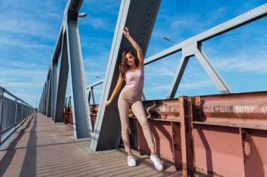 Gün batımında nehrin üzerindeki eski paslı nakliye köprüsünde poz veren genç ve güzel bir kadının ılık yaz portresi..