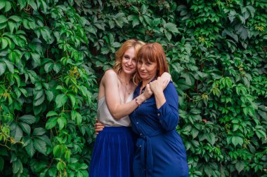 Güzel anne ve yetişkin kızı bir yaz günü yeşil bir arka planda birbirlerine sarılıyorlar.